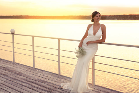 beautiful bride in a cream satin dress, with the sun setting behind her