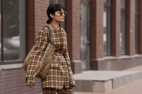 a very fashionable woman in sunglasses wearing a checked brown suit and snakeskin handbag