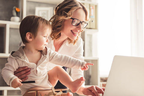 a woman working on her laptop while holding her young son
