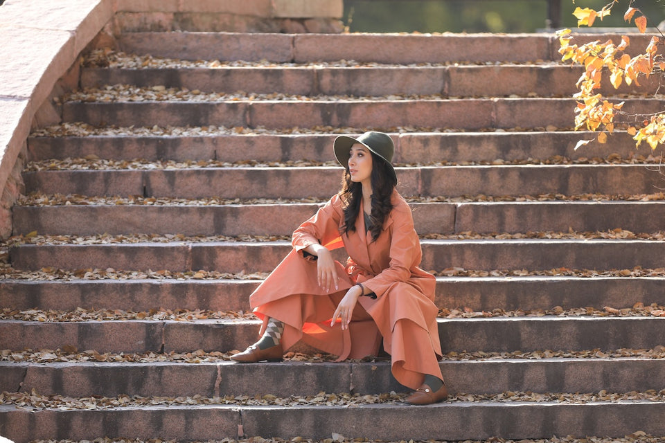 a woman sitting on steps wearing a hat and a terracotta colored coat with matching pants