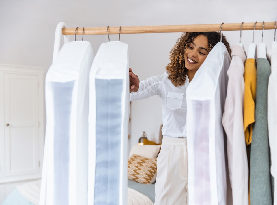 a woman sorting through her clothing and Hayden Hill Garment Bags on a hanging rail