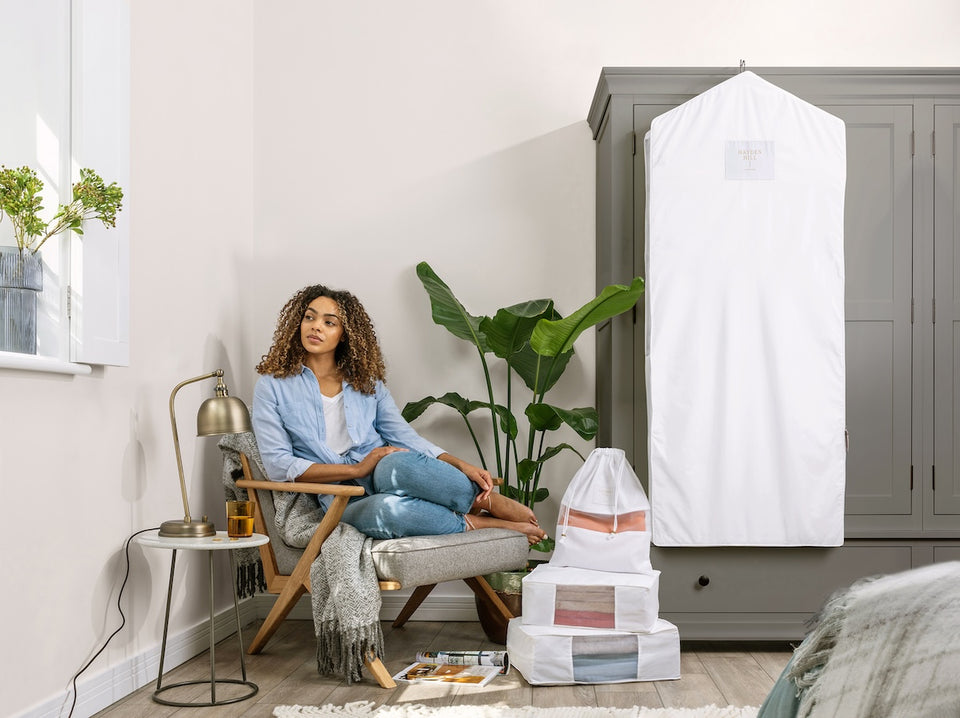 a woman sitting on a chair next to Hayden Hill storage bags, a dust bag and a long garment bag hanging on her wardrobe