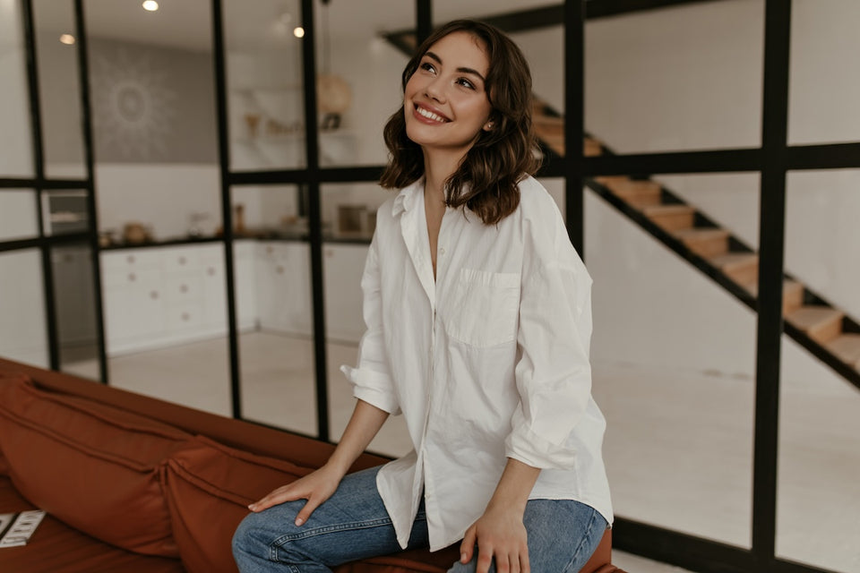 a woman sitting down wearing a classic white shirt and denim jeans