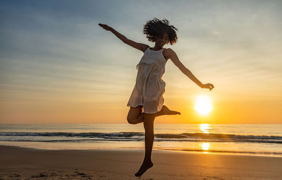 a woman dancing with happiness in a light summer dress with the sun setting behind her