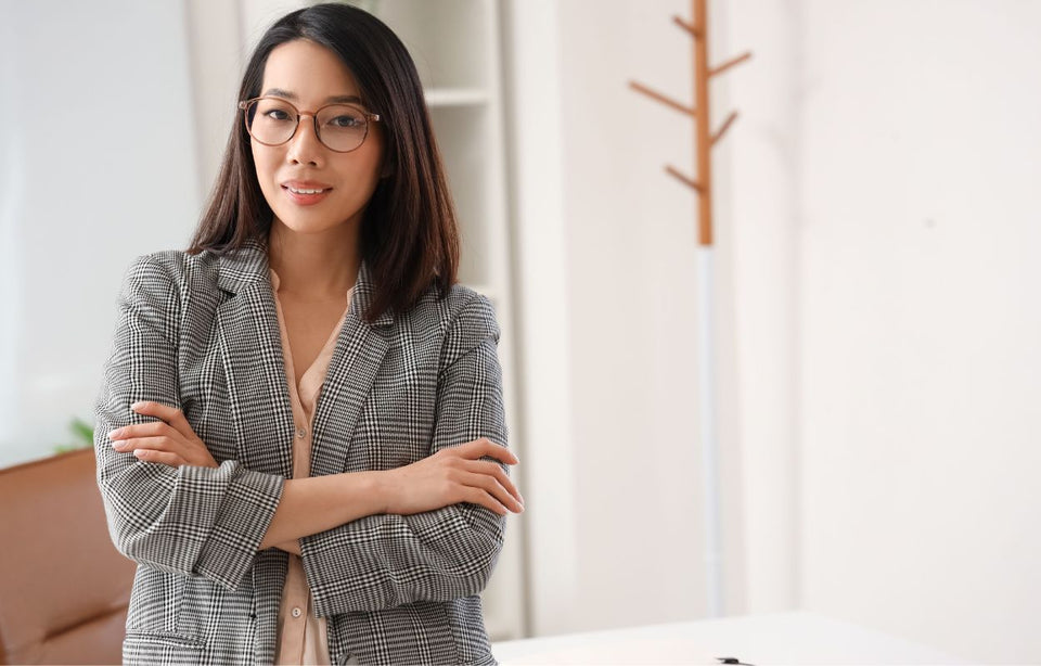 a woman in her office wearing a black and white check blazer over a pastel pink shirt