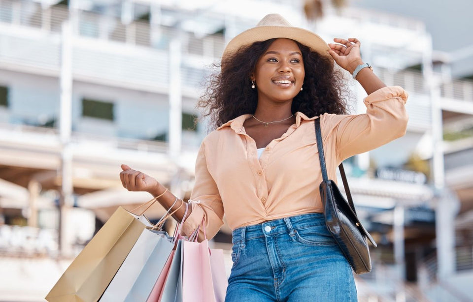 a woman wearing jeans an apricot colour shirt and a straw hat carrying several shopping bags