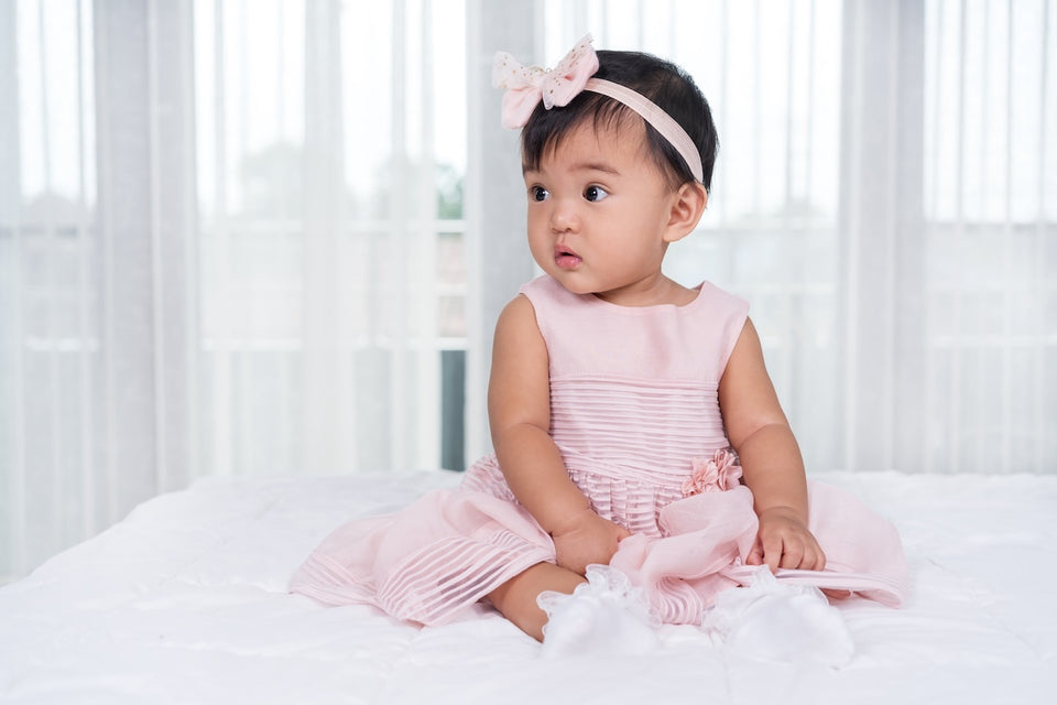 a gorgeous baby wearing in a pale pink dress with a matching bow hair band