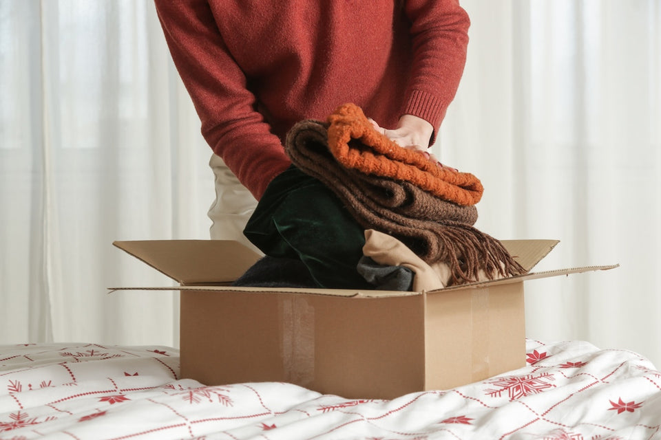 a close up of a woman placing winter clothing into a cardboard box