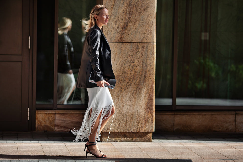 a fashionable woman walking down the street in a black leather jacket, a fringed skirt and sandals