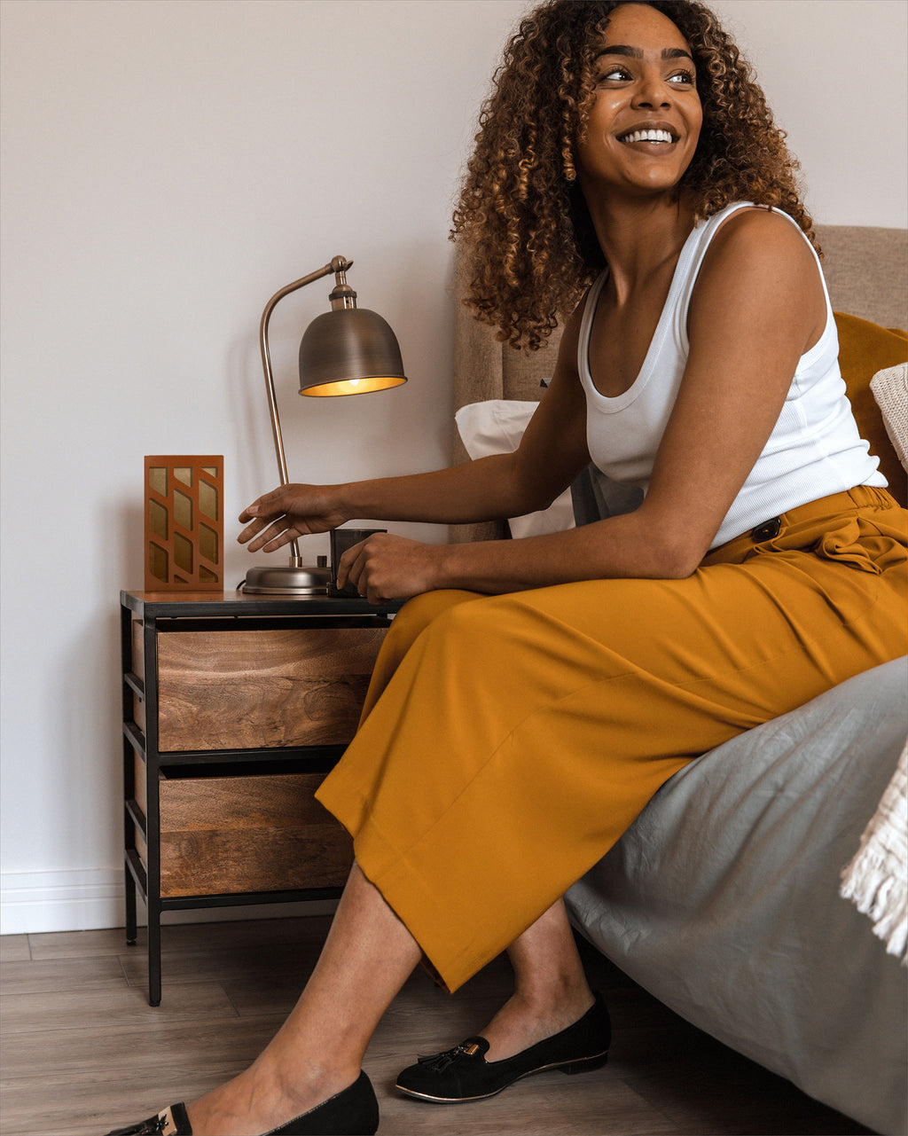 a smiling woman sitting on her bed with a moth trap placed next to her on the side table