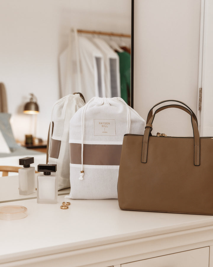 a Hayden Hill dust bag sitting next to a brown handbag on a dressing table