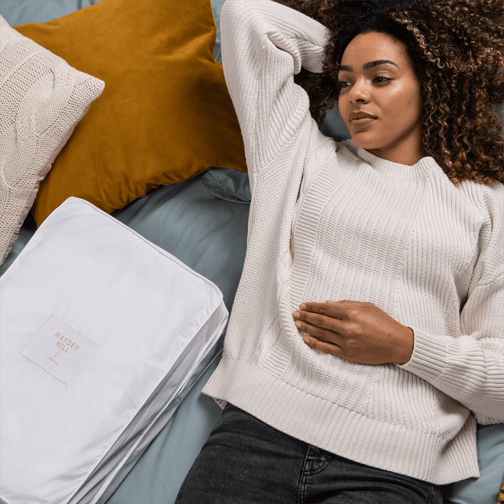 a woman lying on a bed surrounded by cushions and a storage bag