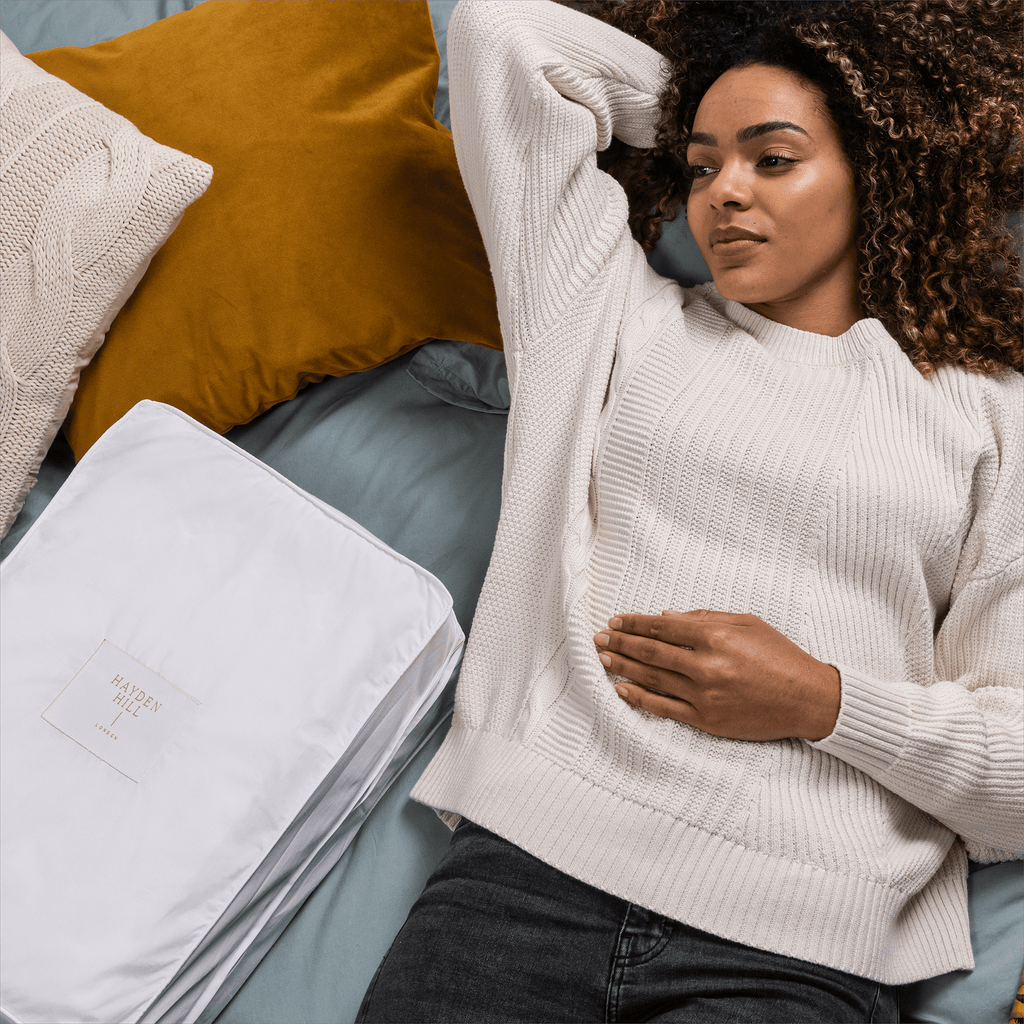 a woman lying on a bed surrounded by cushions and a storage bag