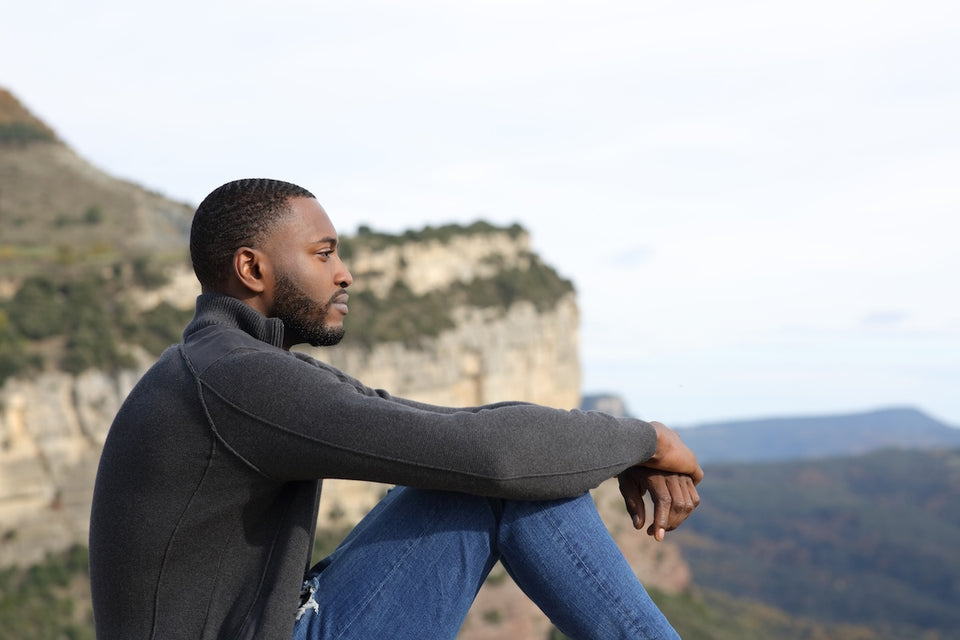 a man sitting by cliffs wearing a knitted top and denim jeans