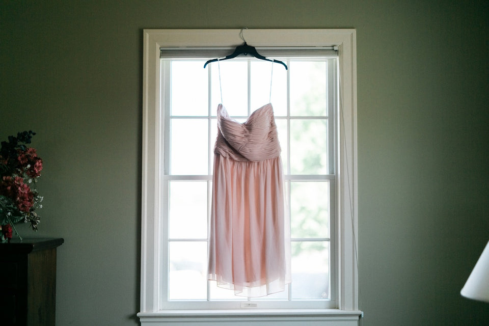 a pale pink sleeveless dress hanging on a window frame indoors