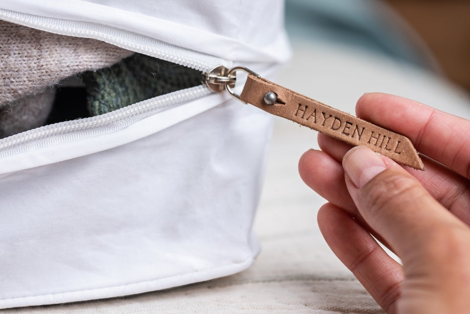 a close up of a Hayden Hill organic cotton storage bag with a hand holding the leather removable zipper pull