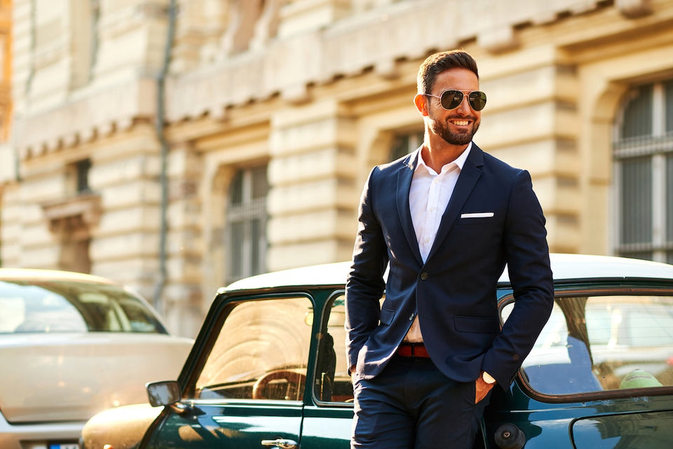 a man leaning on a car, wearing navy blue suit and sunglasses