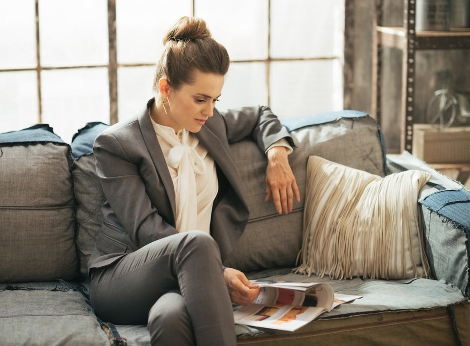a woman, seated on a sofa, wearing a tailored jacket and pussybow shirt with smart trousers