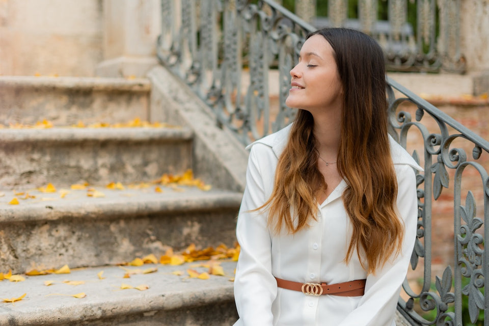 a woman wearing a white blouse sitting on the steps in autumn sunshine