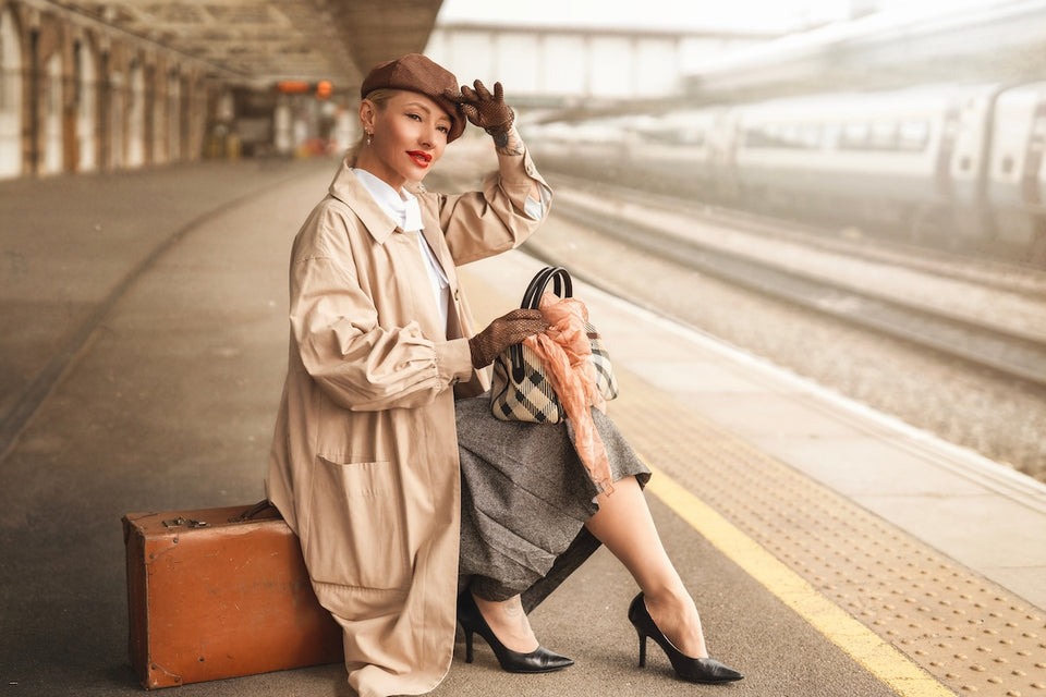 a stylish woman at the train station wearing vintage clothes and holding a bag with a scarf tied around it