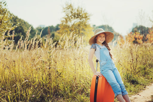a young girl in a sunny field, leaning on a suitcase