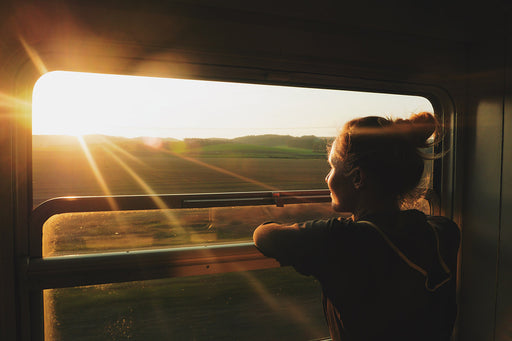 a woman looking at the countryside at sunset through a train window