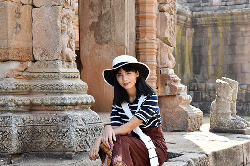 beautiful woman wearing a striped top and patterned skirt sitting outside an ancient temple