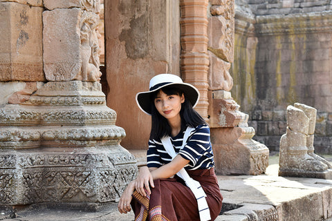beautiful woman wearing a striped top and patterned skirt sitting outside an ancient temple