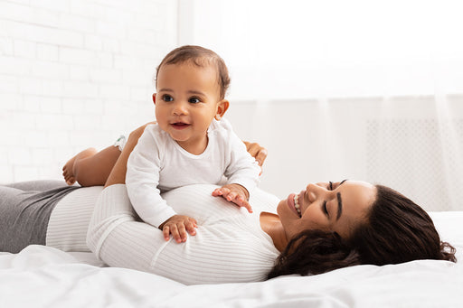 a gorgeous smiling baby lying on his mother’s tummy on their bed