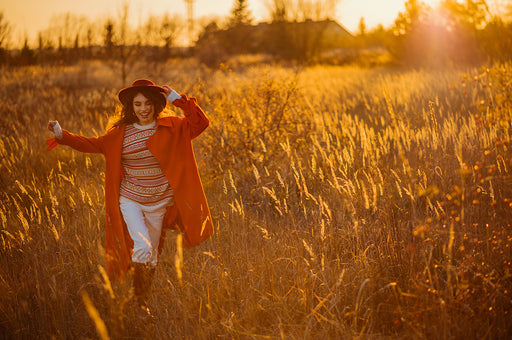 a woman in an orange coat and patterned sweater running through a golden field of grasses