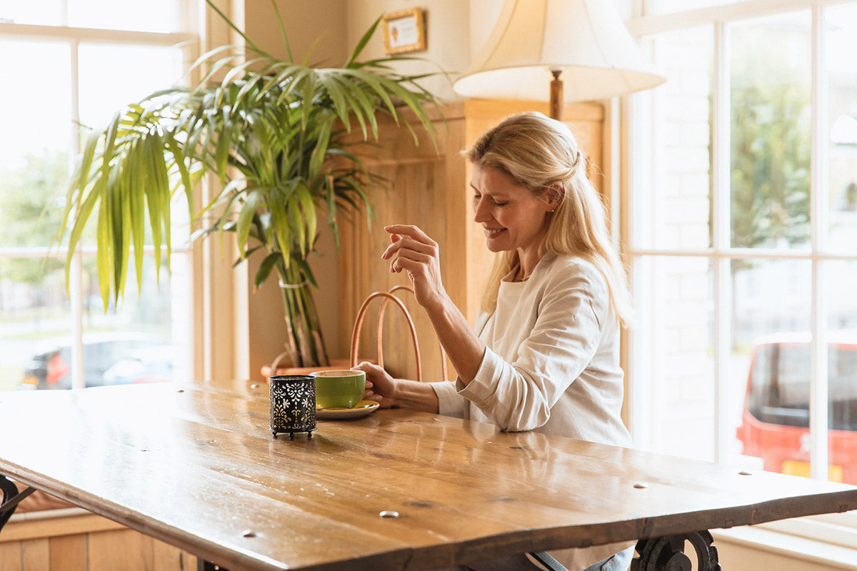 Blonde lady wearing a classic linen jackets sitting at a table having coffee