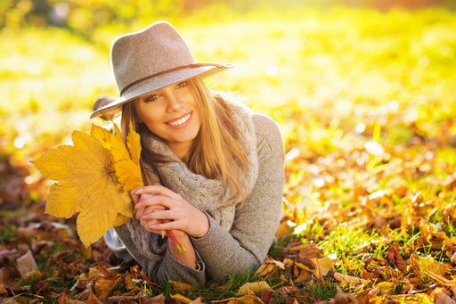a beautiful smiling woman lying in golden leaves, wearing light woollens