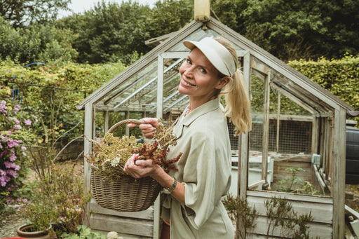 a beautiful woman in the garden wearing a linen outfit and holding a basket of dried flowers
