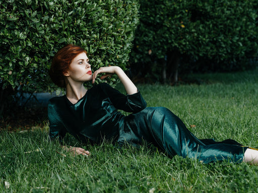 a glamorous woman wearing a green velvet dress lying in green grass