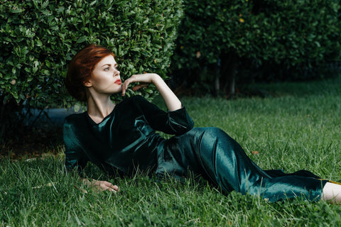a glamorous woman wearing a green velvet dress lying in green grass