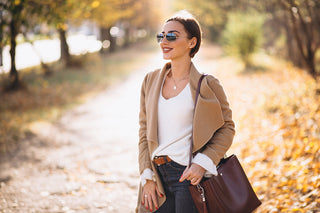 a stylish woman standing in the autumn sunshine, dressed in a relaxed overcoat with a large tote