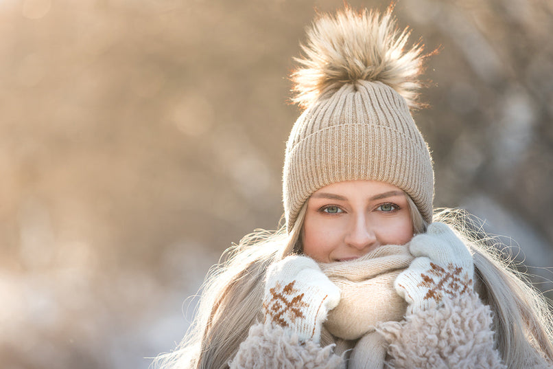 a woman dressed in a pom pom beanie, thick woolen gloves and a scarf to keep out the cold