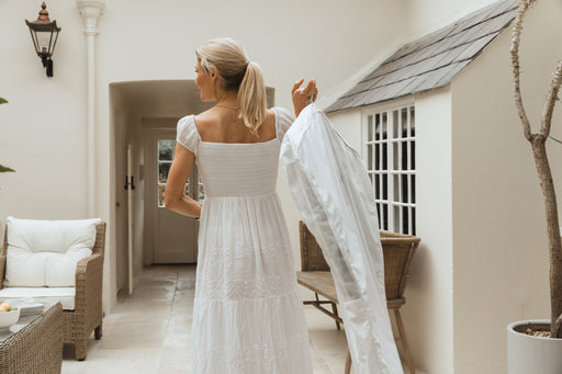 a woman in a pretty white dress carrying a white garment storage bag over her shoulder