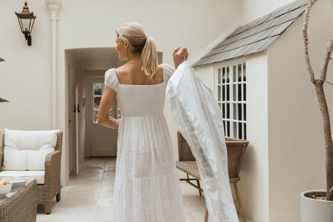 a woman in a pretty white dress carrying a white garment storage bag over her shoulder