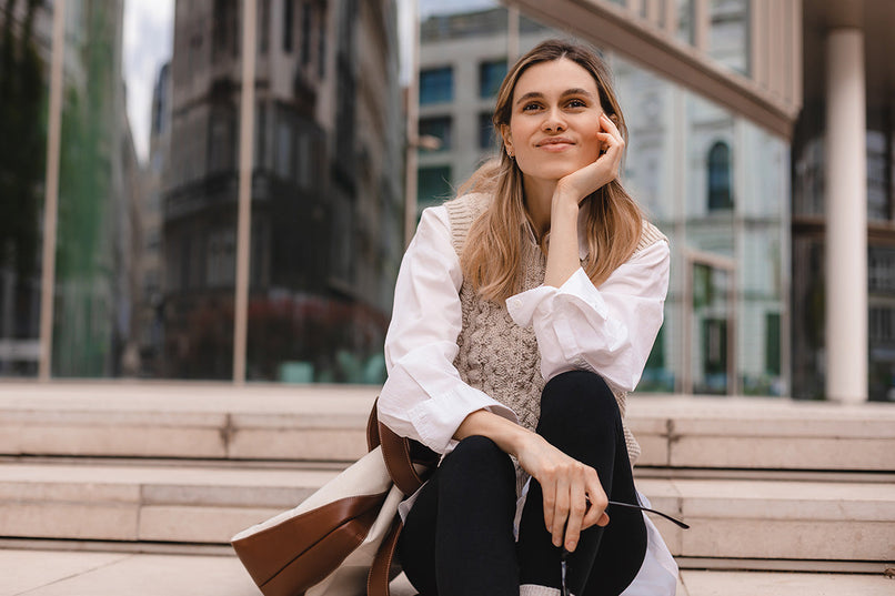 a woman sitting on steps dressed in a casual white shirt, chunky knit vest and leggings