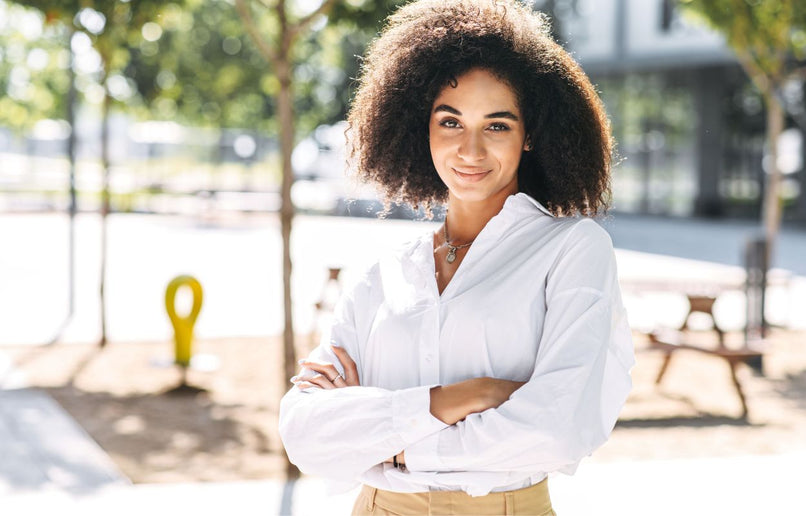 a woman standing outside wearing a white shirt and sand coloured pants