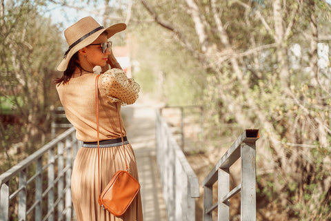 a woman wearing a hat and dressed in caramel-coloured vest and pleated skirt