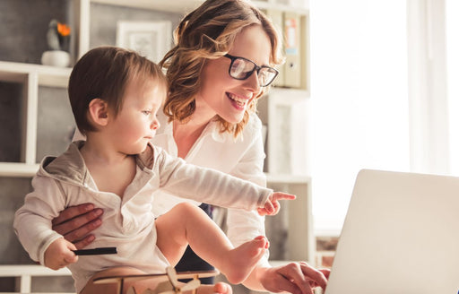 a woman working on her laptop while holding her young son