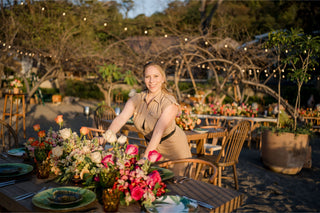Lauren Grech arranging a vibrant floral wedding dining table outdoors with string lights in the background