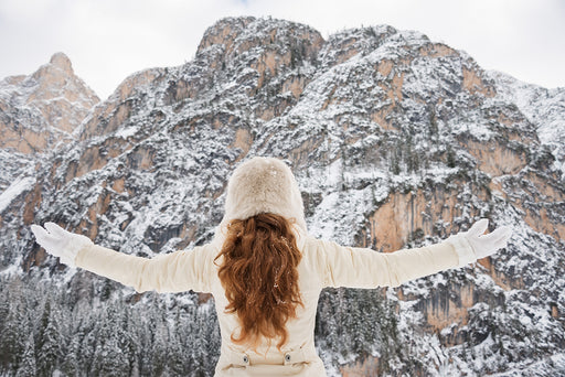 the back view of a woman wearing all white standing in front of a snowy mountain scene