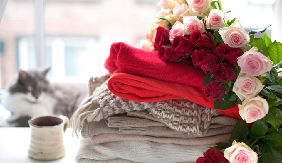 A pile of woolen sweaters and scarves topped with beautiful red and pink roses