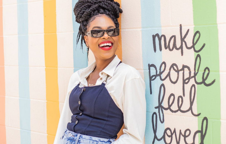 Kat leaning against a brightly painted wall with the wording "make people feel loved"