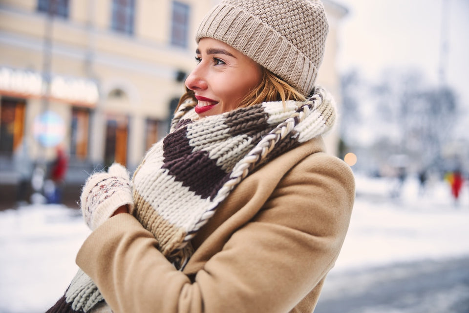 a woman looking cosy in a camel coat with woollen gloves, scarf and hat