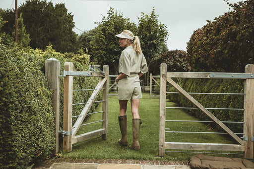 a blond woman in a khaki linen playsuit wearing rain boots