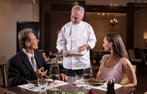 a chef at a restaurant talking about his dish with a couple of dinner guests waiting to be served